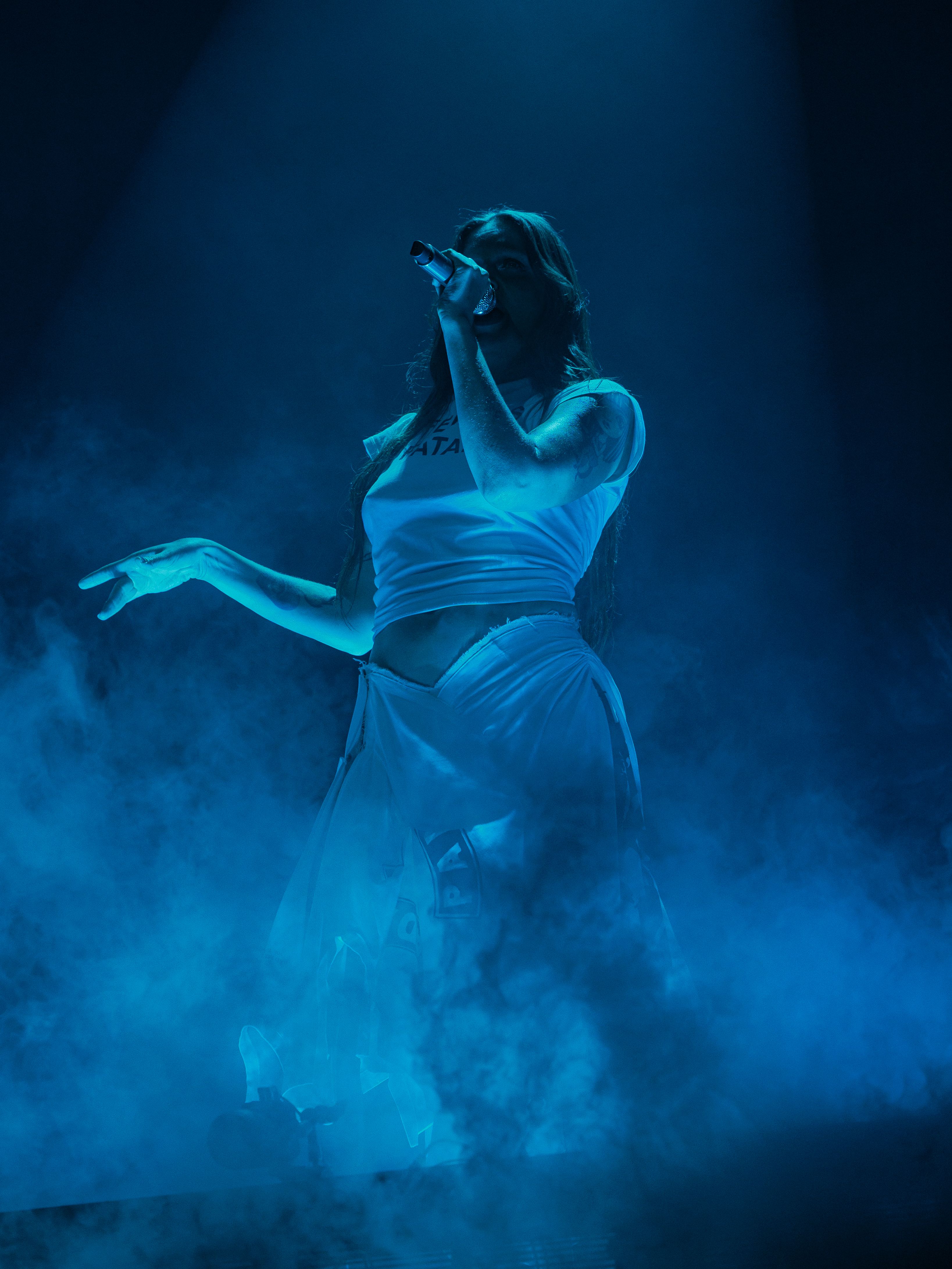 Tove Lo stands in dense blue stage haze while singing into a handheld microphone at the Greek Theatre.