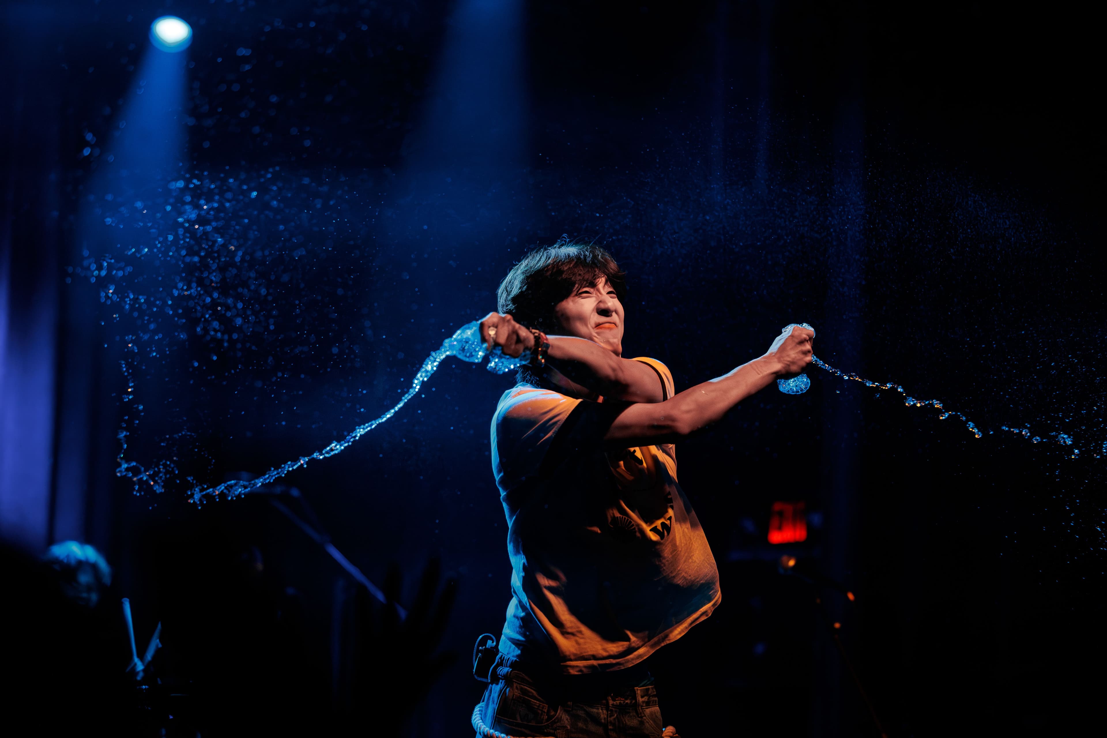 HOHYUN swings two water bottles across the stage, sending streams of water through blue light at the El Rey Theatre.