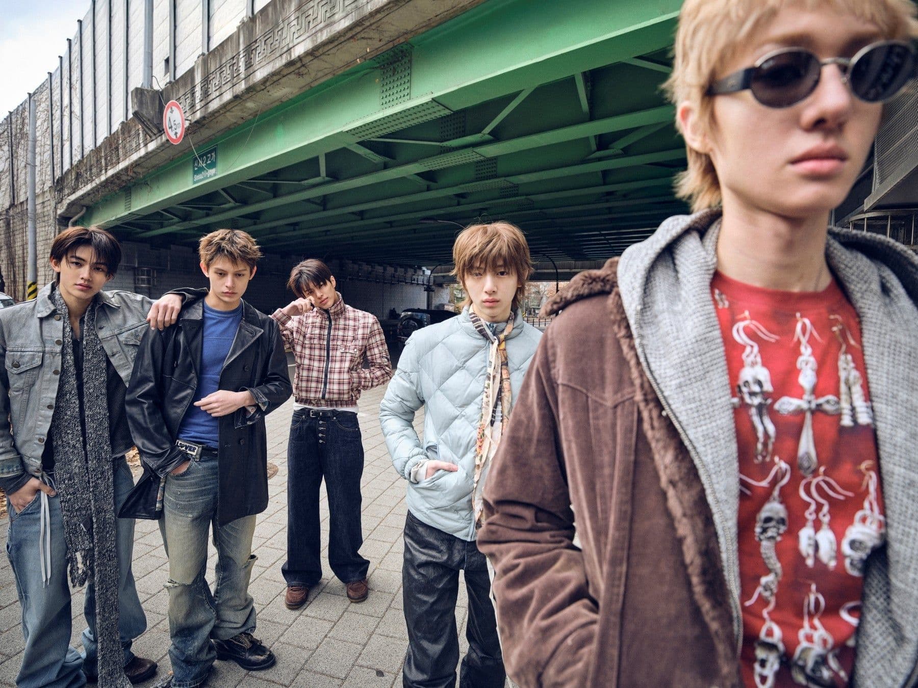 The five members of CORTIS pose beneath a green overpass in layered streetwear.