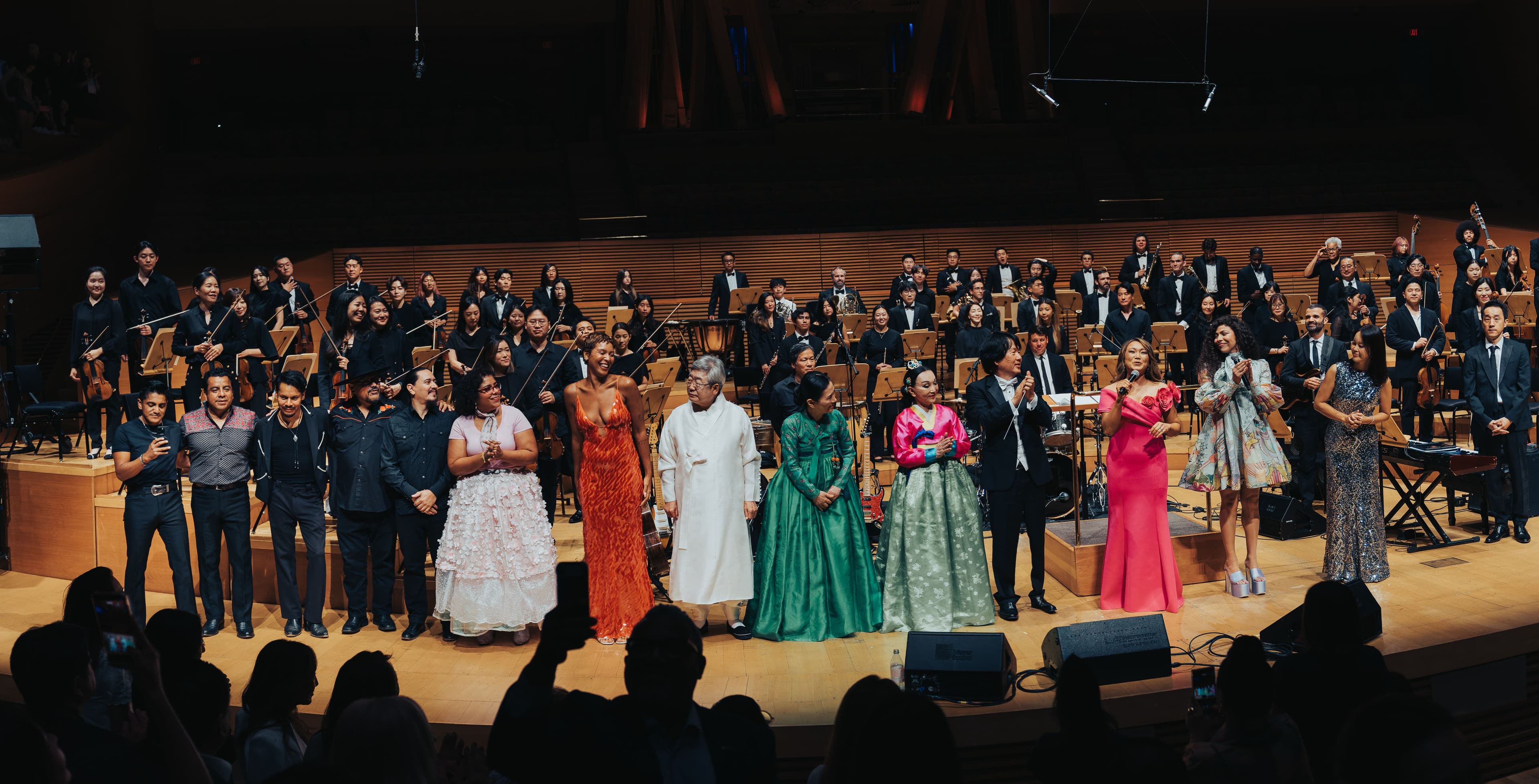 Performers, musicians and hosts gather across the stage with the orchestra behind them at Walt Disney Concert Hall.