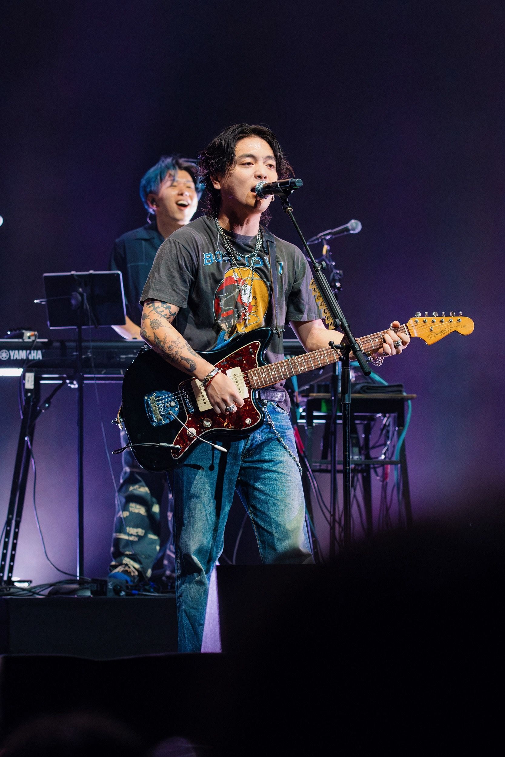 Yuuri sings into a stand-mounted microphone while playing an electric guitar, with a keyboardist behind him at The Wiltern.