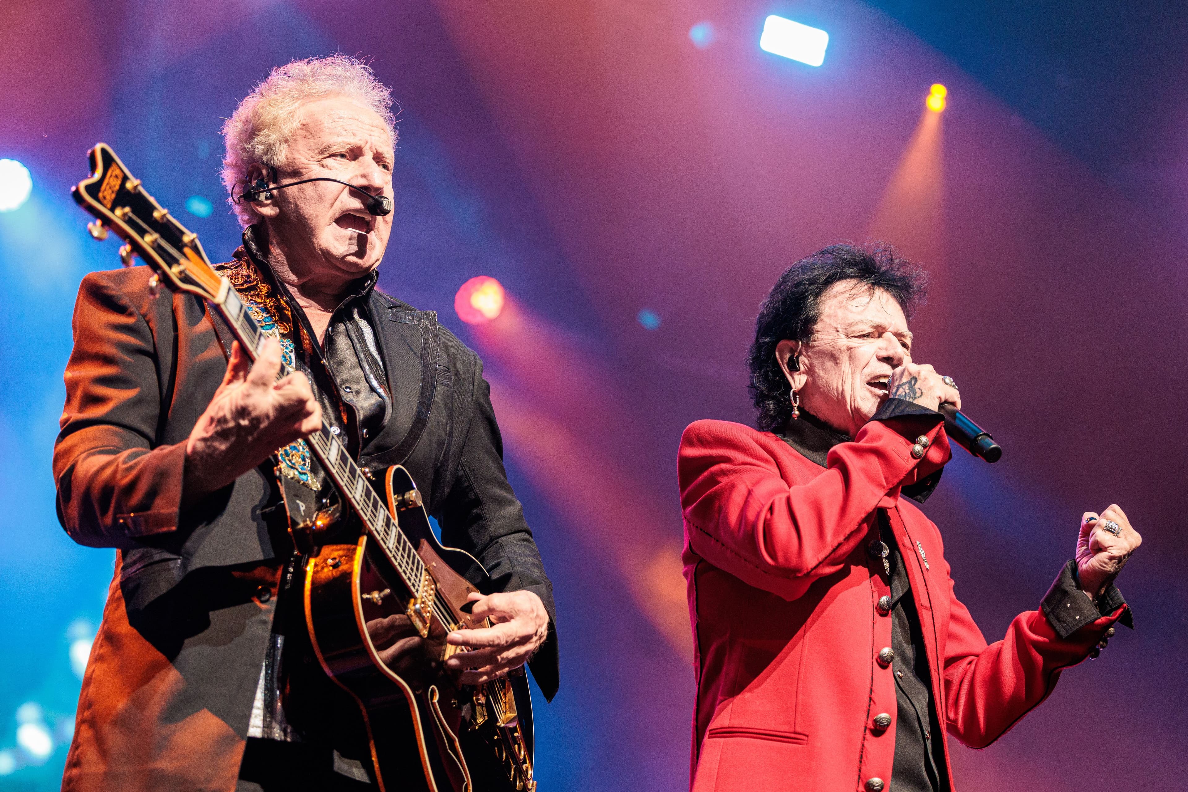 Graham Russell plays guitar beside Russell Hitchcock as Air Supply performs beneath colorful stage lights at YouTube Theater.