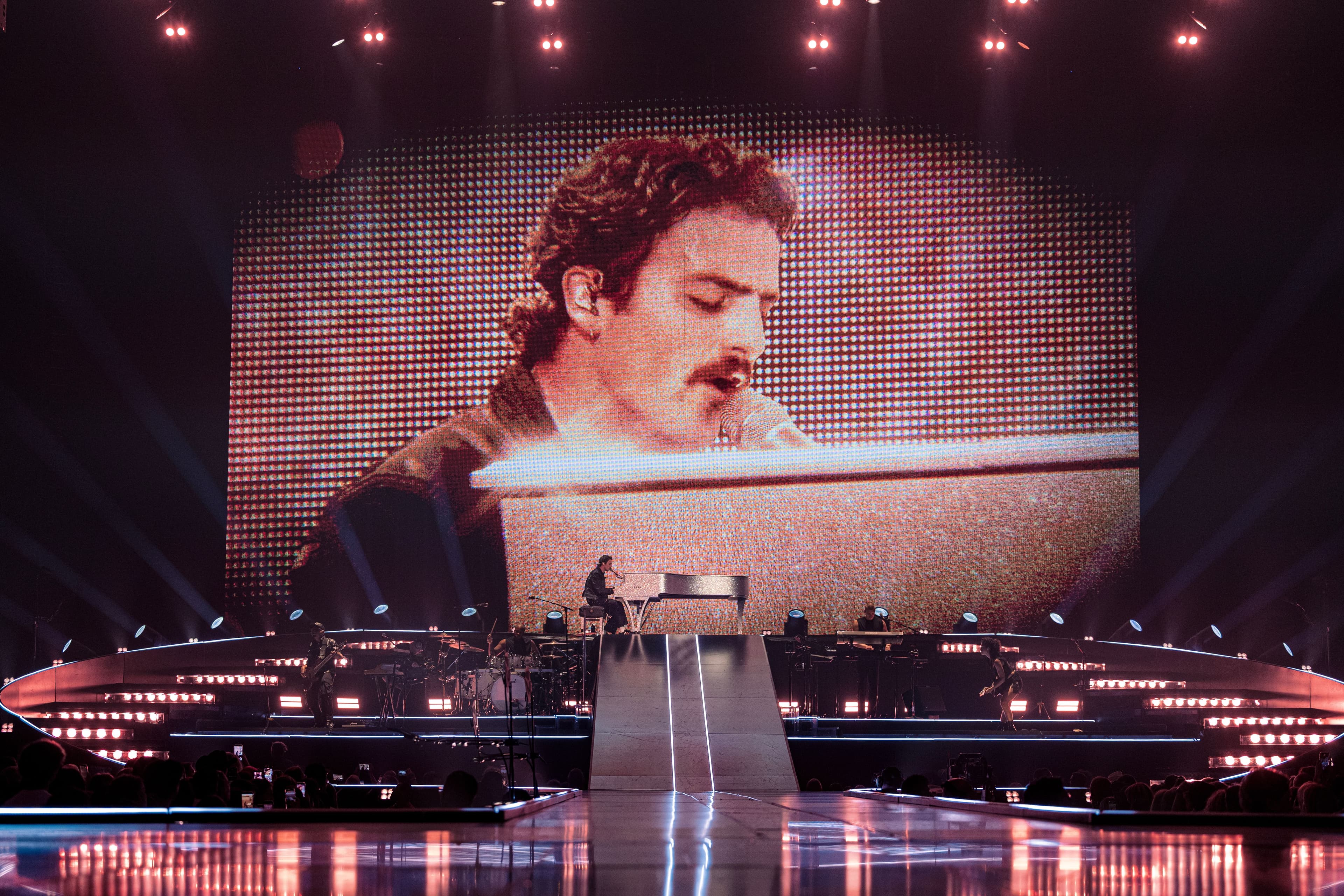 Benson Boone sits at a piano on the main stage while an enormous screen behind him projects a close-up of his performance.