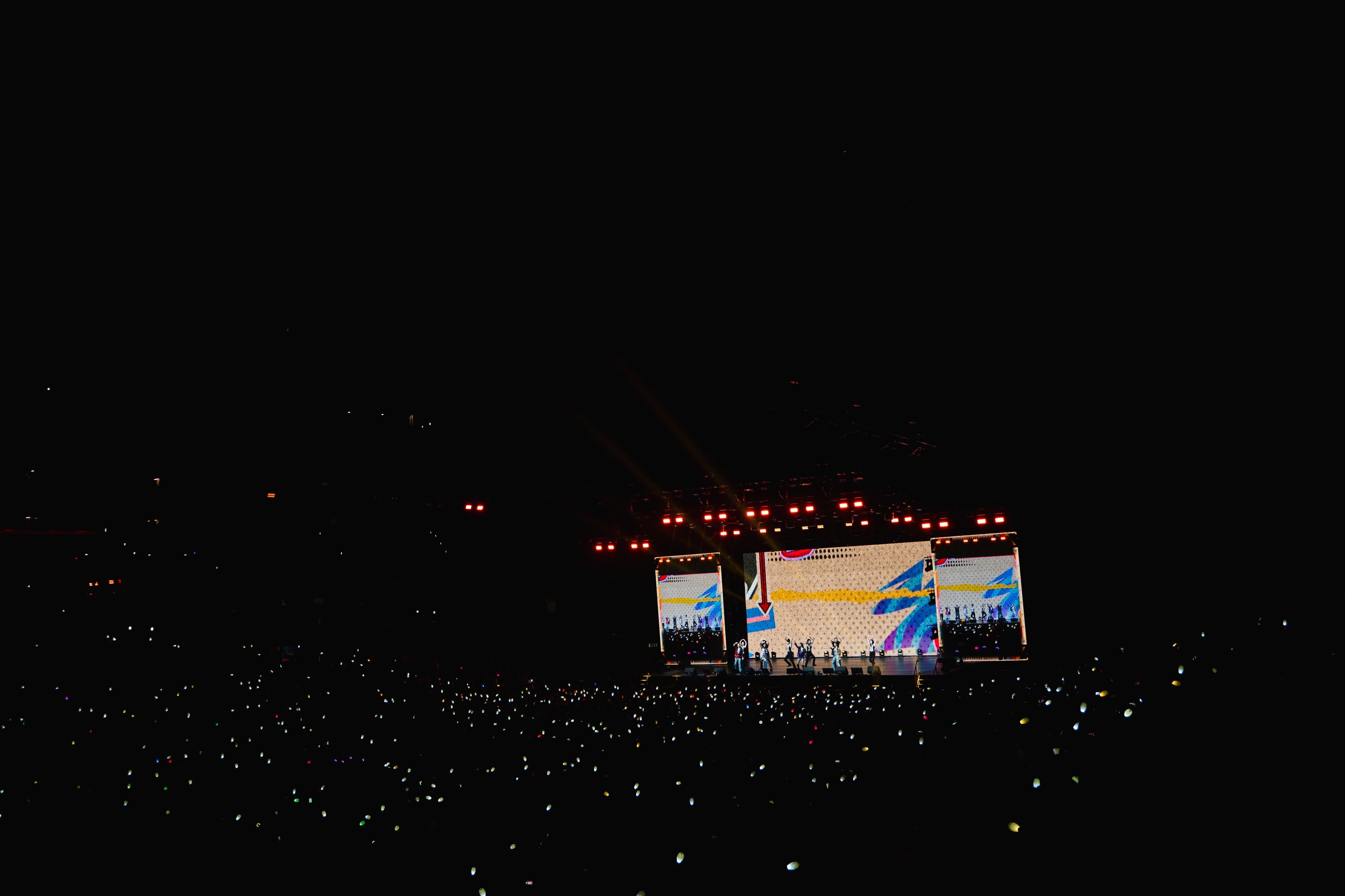 MAMAMOO performs on a brightly lit stage in the distance as thousands of light sticks glow throughout the darkened Crypto.com Aren