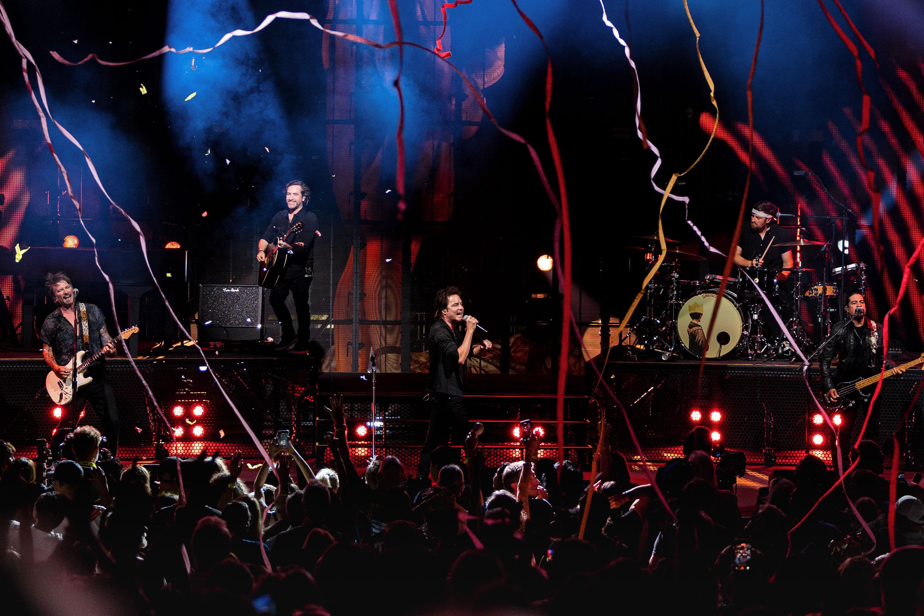 Train performs across the Greek Theatre stage beneath red and white streamers as the crowd watches.