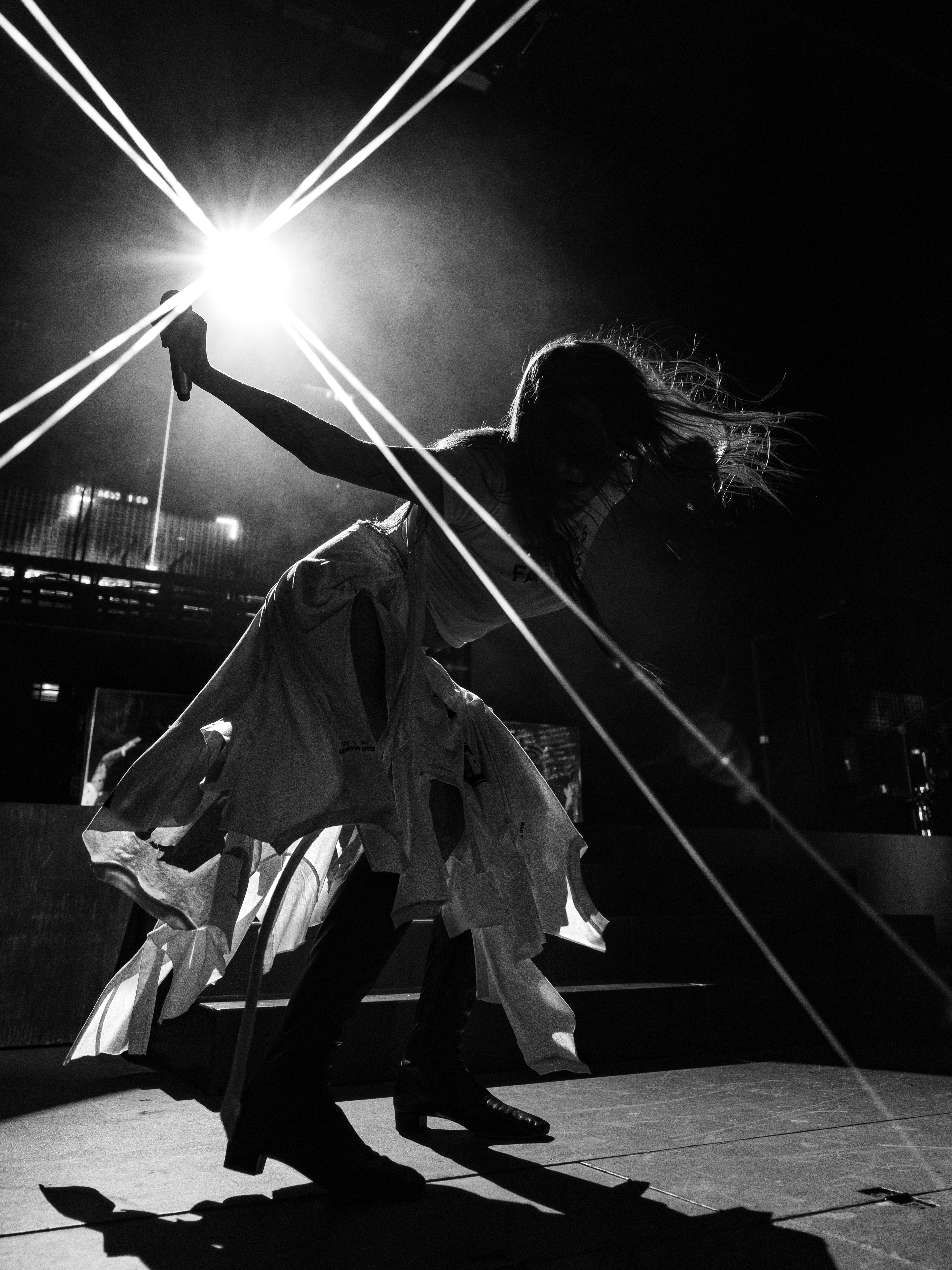 A black-and-white silhouette of Tove Lo leaning forward with a microphone as bright stage lights form diagonal beams behind her.