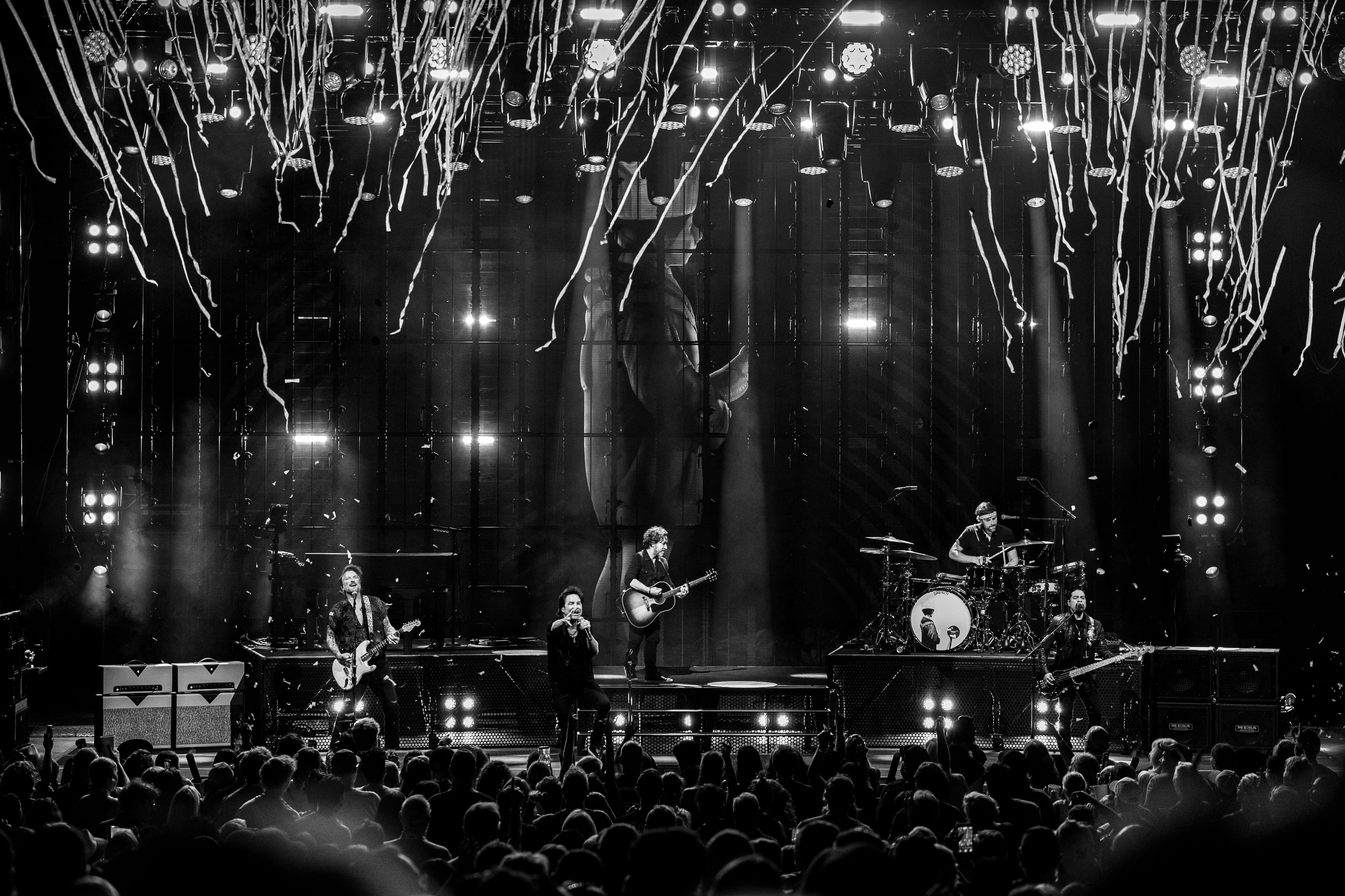 Train performs in black and white beneath hanging streamers and bright stage lights at the Greek Theatre.