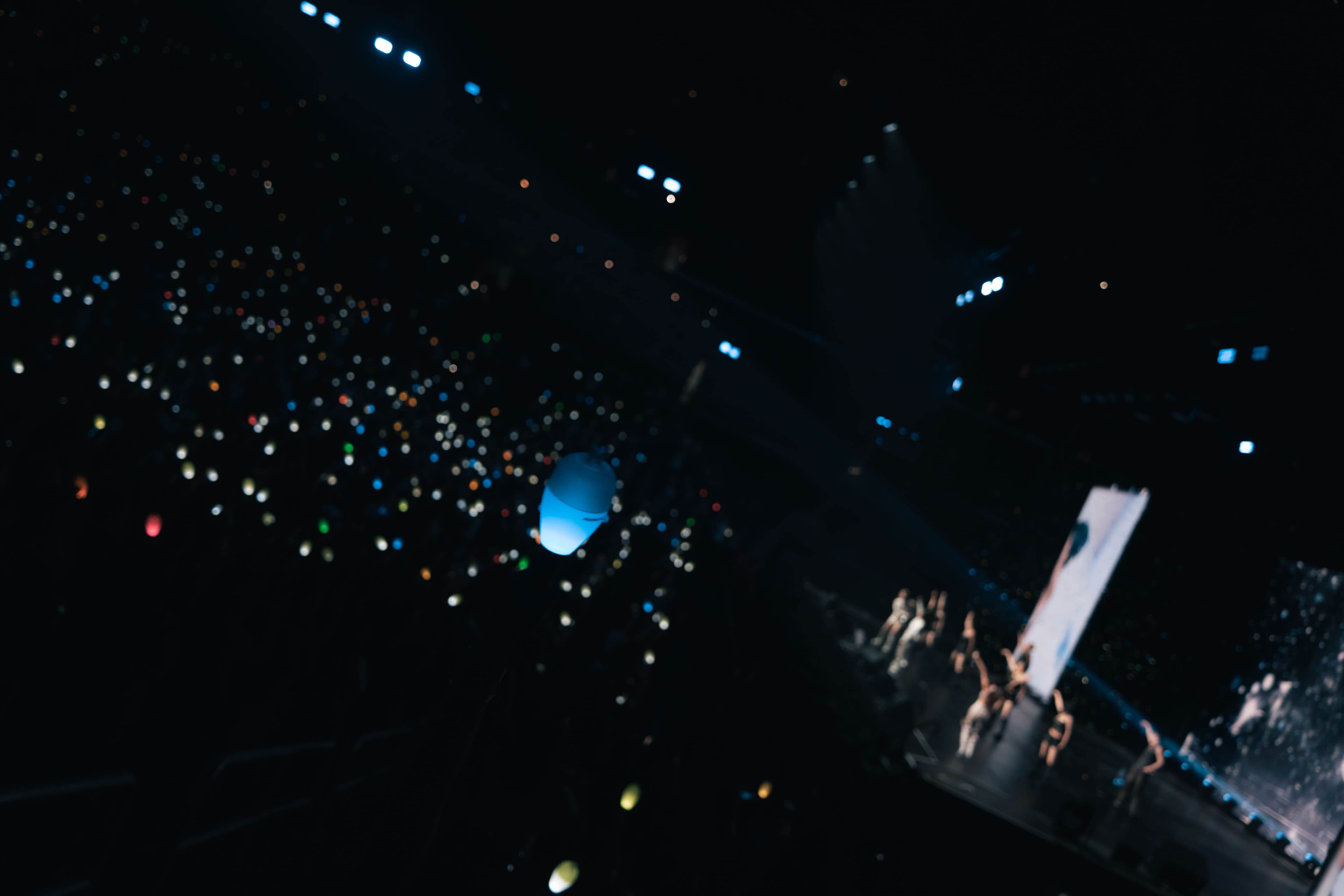 A blue MAMAMOO light stick floats in the foreground as hundreds of lights glow across Crypto.com Arena and the group performs onstage in the distance.