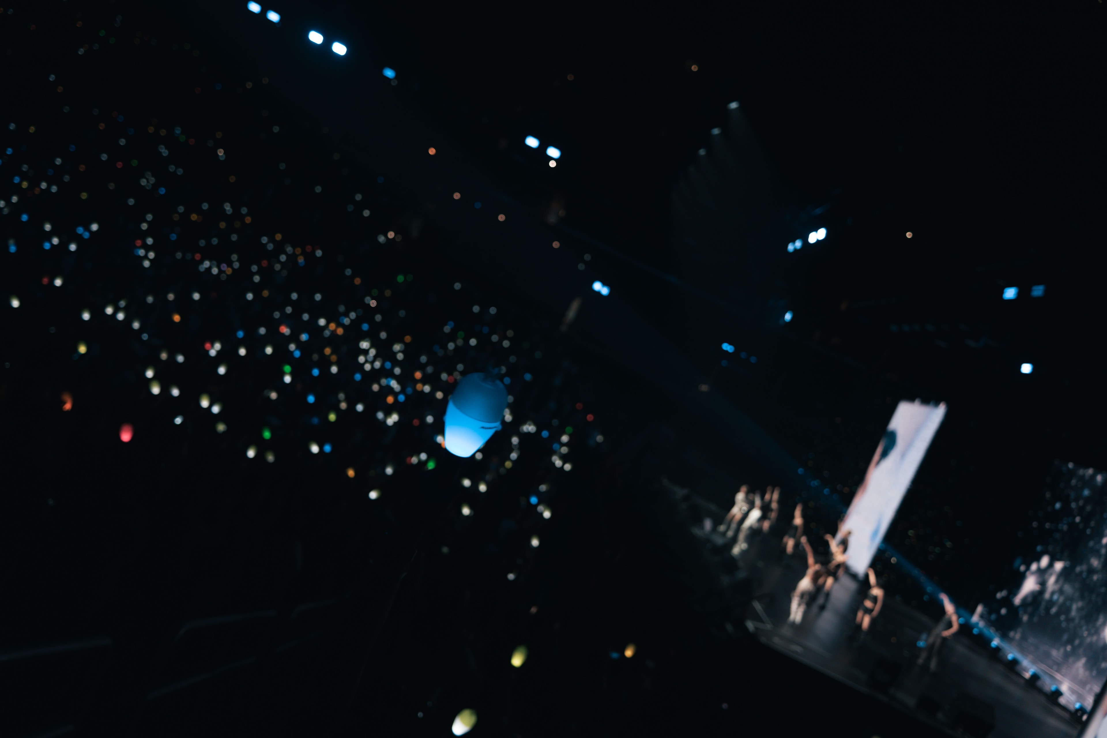 A blue MAMAMOO light stick floats in the foreground as hundreds of lights glow across Crypto.com Arena and the group performs onstage in the distance.
