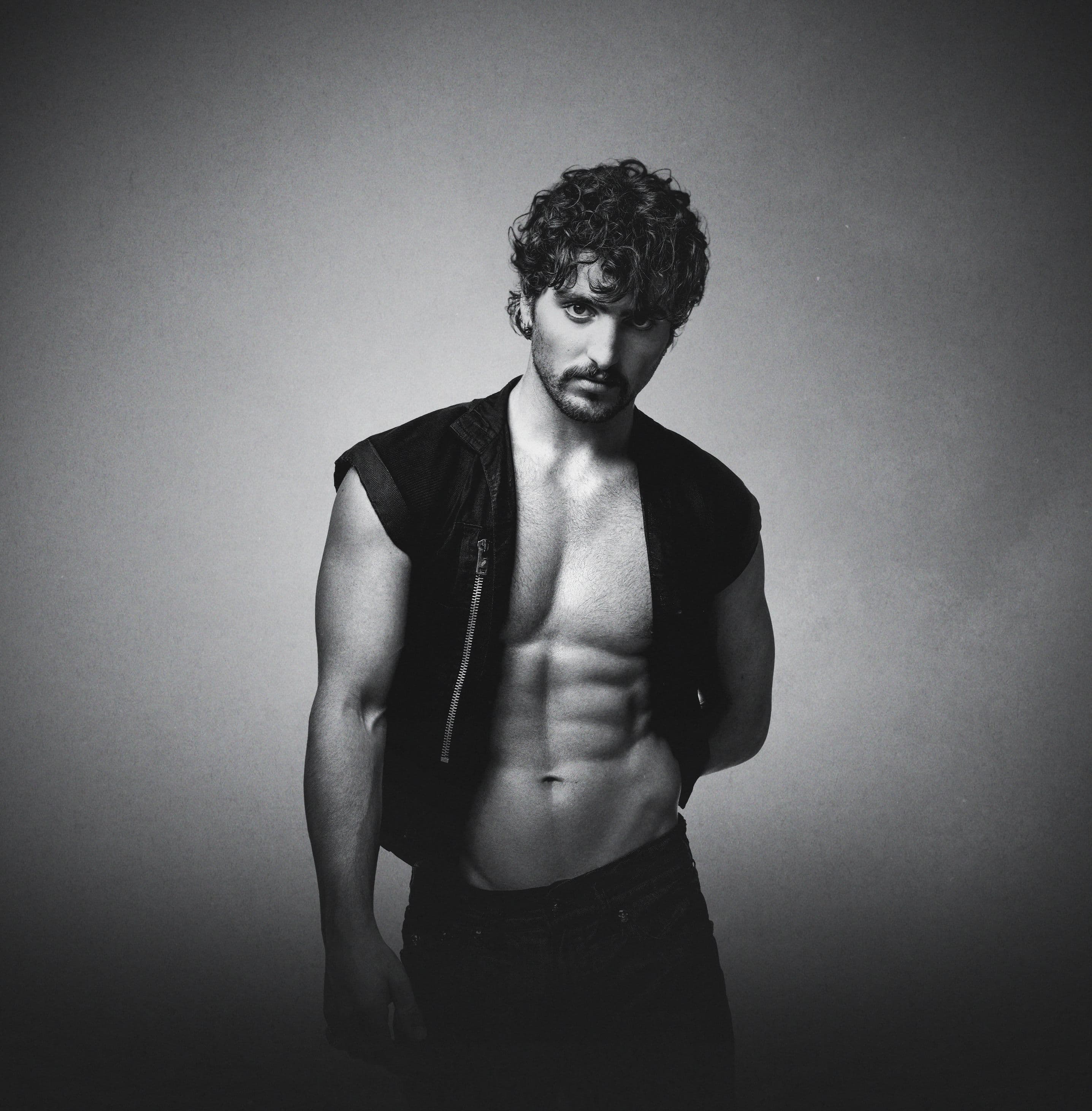 Benson Boone poses in a black-and-white studio portrait wearing an open sleeveless vest.